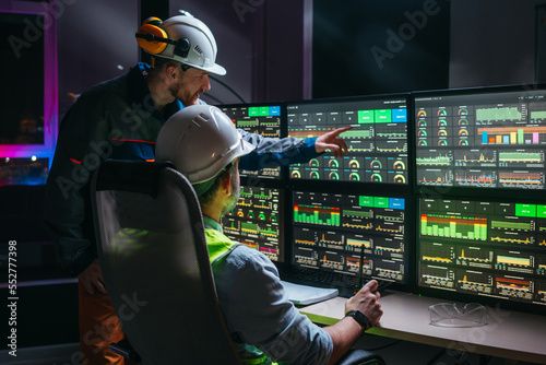 Head engineer and factory operator following product process on factory uses SCADA system and industry 4.0. Two operators controll assembly line using screens with human-machine interface