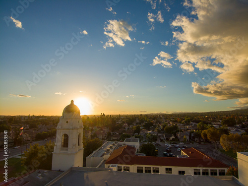 aerial shot of homes, apartments, and shops in the city skyline with cars driving on the street lush green trees and the bell tower at Monrovia High School at sunset in Monrovia California USA