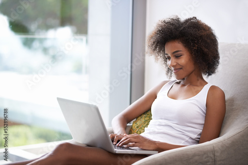 Some early morning catching up with a friend. Shot of a beautiful young woman in pajamas using a laptop.