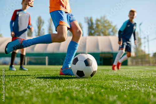 Closeup boy kicking ball while playing football with teammates