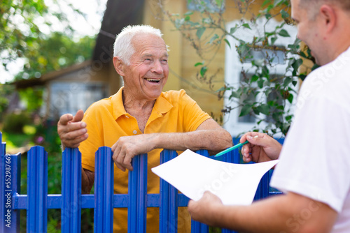 Grandfather talking to census agent standing at fence of his country house