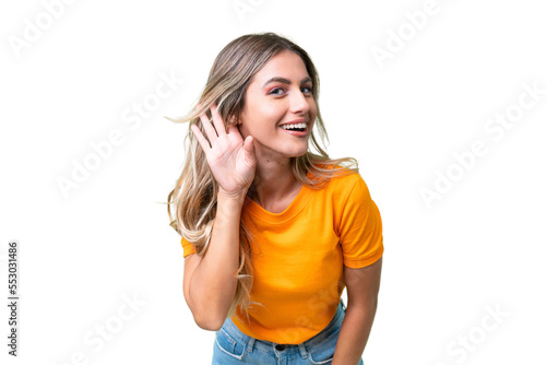 Young Uruguayan woman over isolated background listening to something by putting hand on the ear