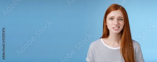 Displeased young awkward redhead girl cringe full disbelief smirking frowning confused look questioned doubtful hearing nuisance dumb story standing blue background uncertain