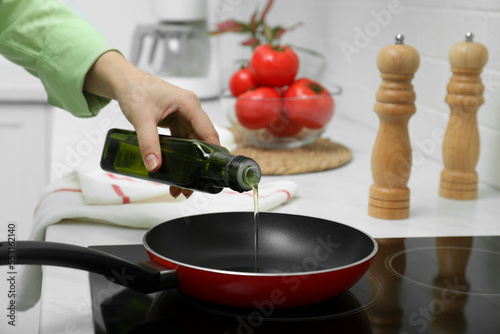 Woman pouring cooking oil from bottle into frying pan in kitchen, closeup
