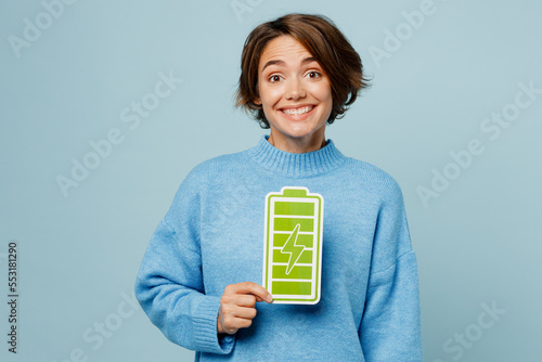 Young positive happy fun caucasian woman wear knitted sweater look camera hold in hand full battery charge green card sign isolated on plain pastel light blue cyan background People lifestyle concept.