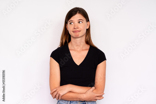 Portrait of young woman looking away with scorn over white background. Caucasian lady wearing black T-shirt and jeans standing with folded arms. Mistrust concept