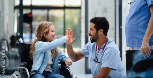 Young multiracial doctor having fun with little girl on wheelchair.