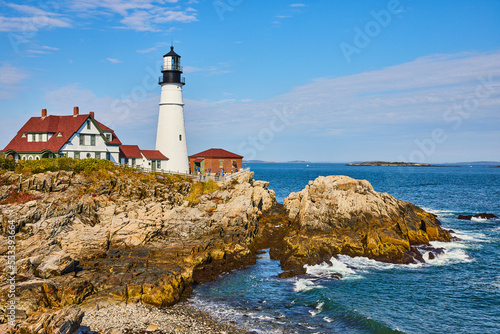 Beautiful white lighthouse in Maine on rocky coastline with ocean waves