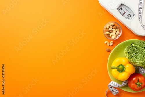 Diet concept. Top view photo of scales tape measure plate with pepper cabbage tomato and nuts on isolated orange background with copyspace