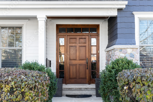 A wooden front door, surrounded by windows, with white, blue, and stone siding.