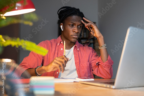 Unhappy sad young African man remote employee feeling tired of monotonous tasks, black guy freelancer doing boring repetitive work, looking at laptop computer screen with upset face, selective focus