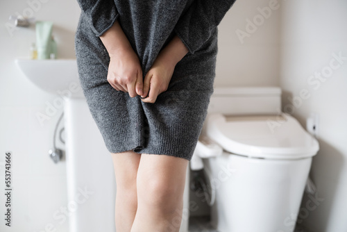 A woman wearing knitwear is complaining of pain from urinary incontinence in front of the toilet