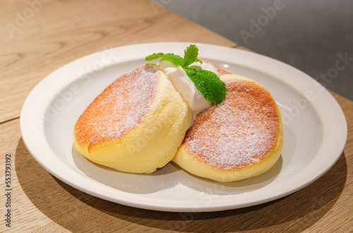 Japanese style sluffy souffle pancake dessert with cream served on a white plate on a wooden table