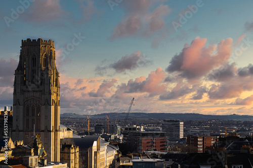 cityscape of bristol uk, showing cranes and a tower, pink couds, blue sky at sunset, with rooftops, busy city