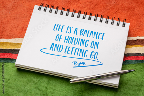 life is a balance of holding on and letting go - Rumi quote, writing in a sketchbook against abstract paper landscape, lifestyle and personal development concept