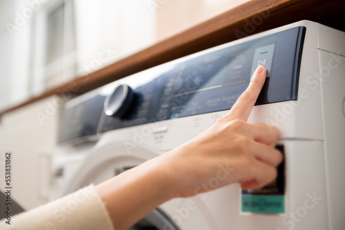 Close-up woman hand pushing washing machine buttons for setting program or start laundry , health care lifestyle concept