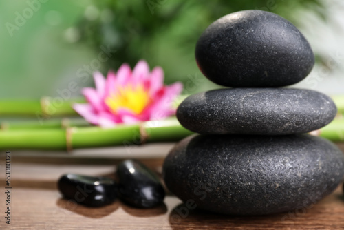 Stacked spa stones, bamboo stems and flower on wooden table against blurred background, closeup. Space for text