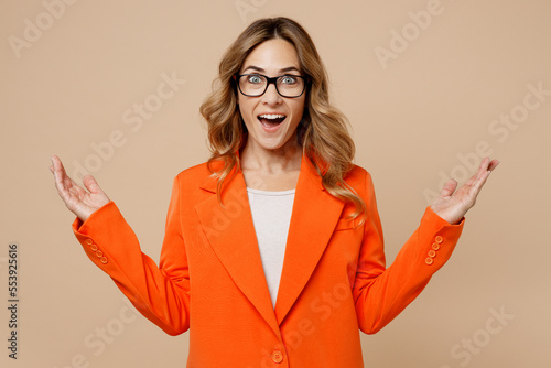 Young successful employee business woman corporate lawyer 30s wear classic formal orange suit glasses work in office look camera spread hands say wow isolated on plain beige color background studio.