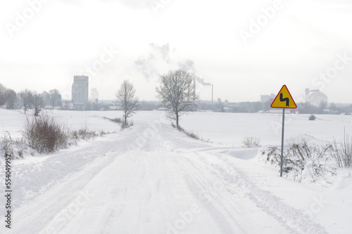 Znak ostrzegawczy, ostry zakręt, zima i ośnieżona droga. Trudne warunki do jazdy.