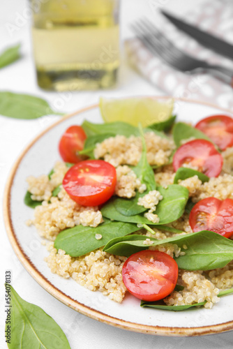 Delicious quinoa salad with tomatoes and spinach leaves served on white table, closeup