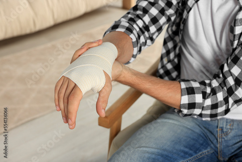 Man with hand wrapped in medical bandage indoors, closeup