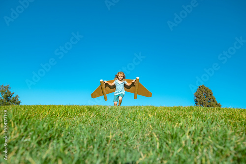 Child boy plays astronaut or pilot. Child on the background of blue sky. Kids with paper wings jetpack dreams. Children imagines dreams of flying. Funny kid with toy jet pack.