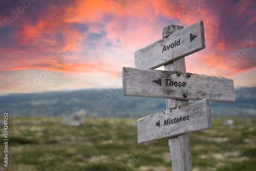 avoid these mistakes text quote engraved on wooden signpost crossroad outdoors in nature. Dramatic pink skies in the background.