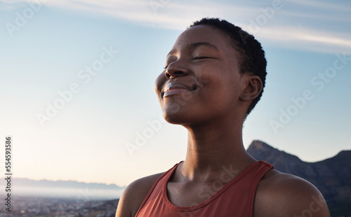 Fitness, calm and breathing of black woman outdoor in nature, mountains and blue sky background for yoga wellness, meditation and zen energy. Face of girl breathing for peace, freedom and mindfulness