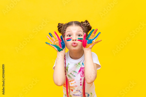A little girl stained in multicolored paints is fooling around. Children's creativity, drawing. Draw with your hands. The art of creating paintings for schoolchildren.