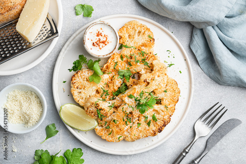 Cauliflower steaks with sauce on white plate, vegetarian dish, view from above