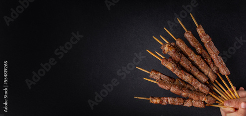 Lamb skewers also called kebabs, or arrosticini or chuan, are small pieces of meat roasted on wooden skewers over charcoal. Black background, banner size, copy space.