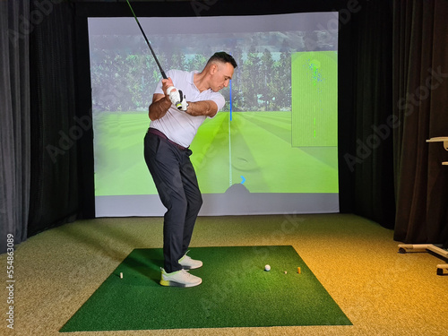 Professional male golfer holding club playing golf indoors on golf simulator