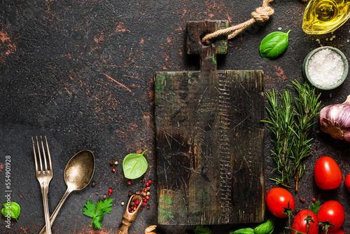 Cooking food composition. Fresh vegetables, spices, herbs and wooden cutting board on black stone background. Top view