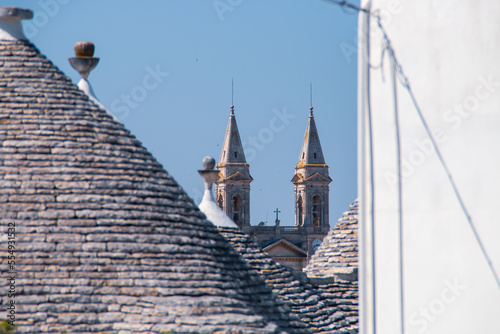 Campanarios de la Basílica santuario de San Cosme y Damián entre tejados de los trullos de Alberobello, Italia. El trullo es una casa con techo cónico de piedra que terminan en un pináculo.