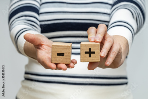 Pros and cons, A woman holds wooden blocks with a positive and negative symbol in her hands, the concept of pros and cons, ups and downs