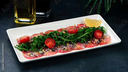 Cold appetizer of beef carpaccio with cherry tomatoes, lemon, arugula, parmesan cheese and pine nuts.