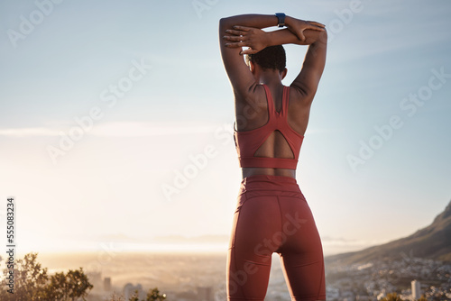 Black woman, fitness and stretching arm on mountain for exercise, workout or training during sunset in outdoors. African American woman in warm up stretch on cliff in sunrise or active life in nature