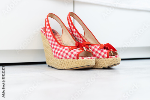 Red White open shoes with a high wedge heel in front of a closet