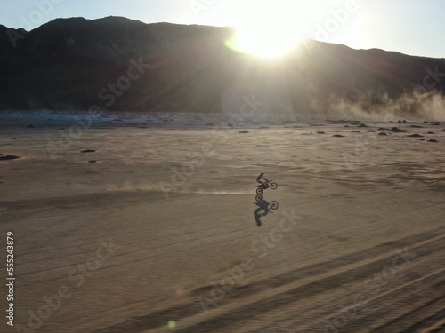 Dirt biker wheelie across dry lakebed in southern California desert at sunset