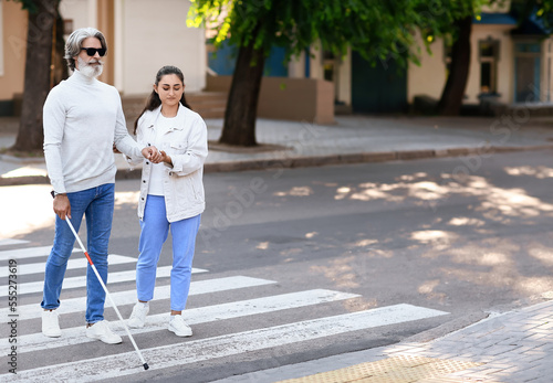 Young woman helping senior blind man to cross road in city