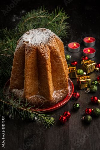 Top view of pandoro sponge cake with sugar, green branches, on dark table with candles and Christmas decoration, black background, vertical, with copy space