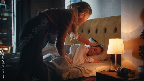 Mother Caring for Her Lovely Daughter, Putting Her to Sleep in Bed Before at Home in the Evening. Babysitter Tucking Little Girl in Blanket and Turning Off Light in Table Lamp.