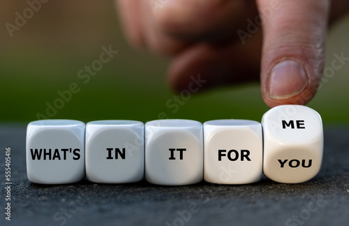 Hand turns dice and changes the expression 'what's in it for you' to 'what's in it for me'.