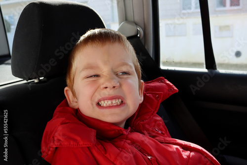 The blond boy wrinkles and grinds his teeth. A cranky five-year-old boy in the cabin of a car. 