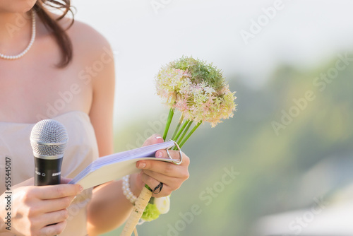 A bouquet of flowers in the hands of a female host, holding a microphone, waiting for the schedule to report the order of the event.