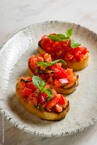 bruschetta with sliced tomatoes cubes and basil on plate on marble table vertical
