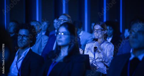 Female Asking a Question to a Speaker During a Q and A Session at an International Tech Conference in a Dark Crowded Auditorium. Young Specialist Expressing an Opinion During a Global Business Summit.