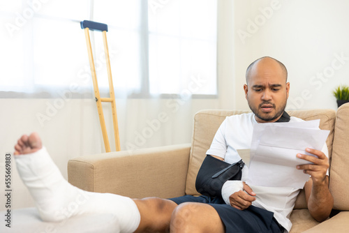 UnHappy man stressed pay invoice medical expenses from accident fracture broken bone injury with leg splints in cast neck splints collar sling support arm. Social security and health insurance.