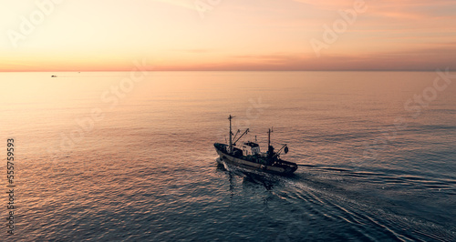 Fishing boat catching fish at sunset aerial view from drone. Small fishing trawler ship on sea surface.