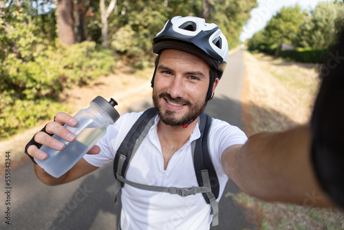male cyclist holding bottle of water and taking selfie
